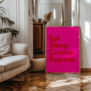 May include: A pink poster with the text "Eat Sleep Create Repeat." in red letters.