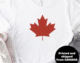 Puede incluir: Camiseta blanca con un gráfico de hoja de arce roja. El texto "Impreso y enviado desde CANADÁ" está impreso en un círculo negro en la esquina inferior derecha de la imagen.