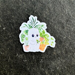 May include: A white ghost with big eyes and a small smile is holding a potted plant. The ghost is surrounded by other potted plants, including a palm tree, a monstera, and a hanging plant. The plants are all in white pots with orange accents.