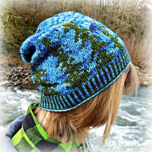 May include: A slouchy knit beanie featuring a variegated pattern of bright blue, dark blue, and olive green yarn. The hat has a ribbed brim and a textured, hand-knitted construction with a soft, relaxed fit that sits comfortably on the head.