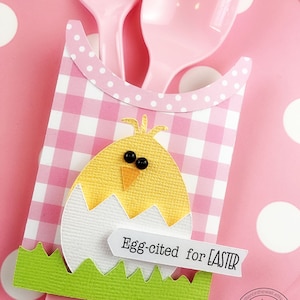 May include: Pink and white checkered Easter themed cutlery holder with a yellow chick design and the text "Egg-cited for Easter".
