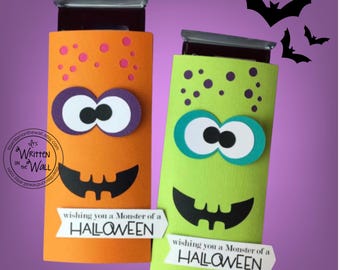 May include: Two rectangular candy bar wrappers featuring orange and lime green cardstock with monster faces. Each has purple or teal eyes, a black jagged mouth, purple polka dots, and a white label reading wishing you a Monster of a HALLOWEEN.
