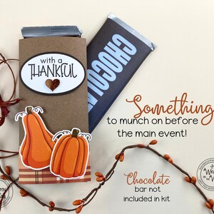 May include: A brown paper gift bag with a chocolate bar inside. The bag is decorated with a pumpkin and the text "with a thankful". The text "Something to munch on before the main event!" is written below the bag. The text "Chocolate bar not included in kit" is written below the text.