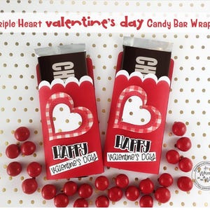 May include: Two red candy bar wrappers with a heart design and the text "Happy Valentine's Day." Each wrapper holds a chocolate bar. Red candies are scattered around the wrappers. The wrappers have a scalloped edge.