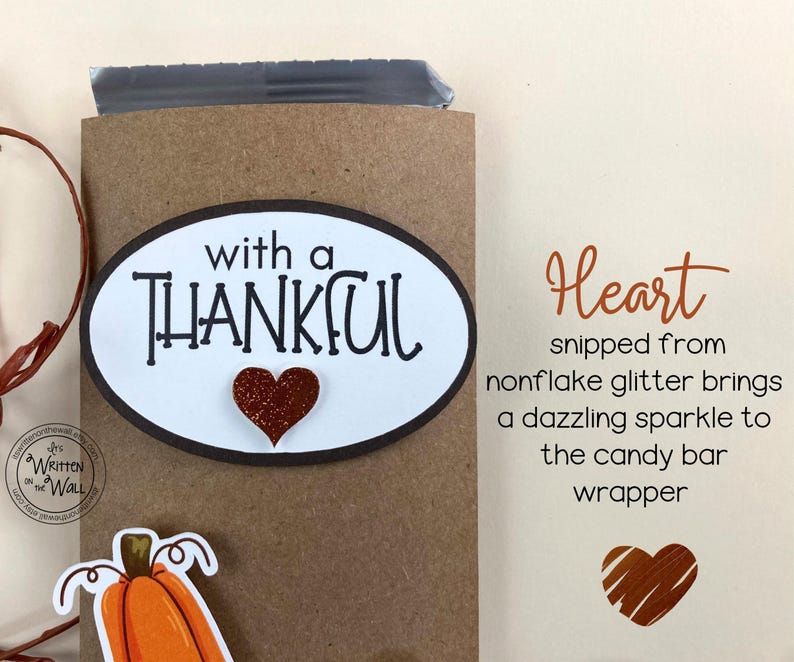May include: A brown paper bag with a white oval sticker that says "with a THANKFUL" with a red glitter heart. The bag is decorated with a brown twine bow. The text "Heart snipped from nonflake glitter brings a dazzling sparkle to the candy bar wrapper" is written on a white background.