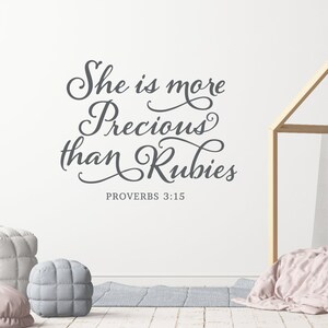 Pode incluir: Uma parede branca com um adesivo de vinil cinza que diz "Ela é mais preciosa do que rubis" com a referência bíblica "Provérbios 3:15" abaixo do texto.