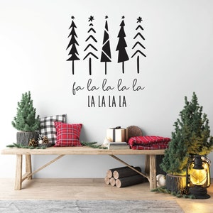 Puede incluir: Un banco de madera rústico decorado para las fiestas con árboles de Navidad en miniatura, cojines a cuadros y una manta a cuadros roja. Una calcomanía de pared presenta árboles de Navidad negros estilizados y el texto "fa la la la la LA LA LA LA."