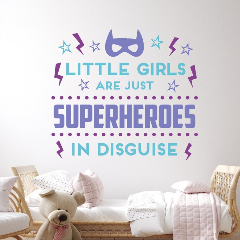 May include: Purple and blue wall decal with the text "Little girls are just superheroes in disguise". The decal features a superhero mask, stars, and lightning bolts.