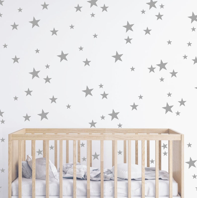 May include: A white crib with a wooden frame and gray star decals on the wall behind it.