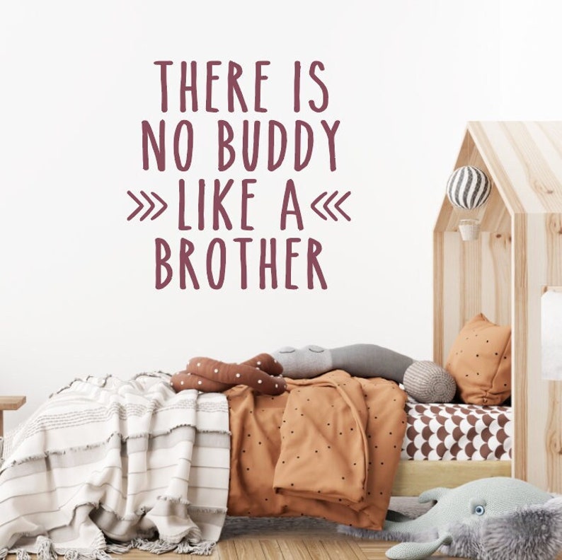 May include: A white wall with a burgundy wall decal that reads "There is no buddy like a brother". The decal is above a bed with a brown and white patterned blanket and a gray and white patterned pillow.
