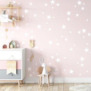 May include: A pink nursery wall with white star decals. The wall has a wooden shelf with a toy airplane and a wooden bunny with a feather hanging from it. There is a wooden dresser with a sign that says "sweet baby love".
