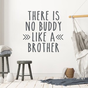May include: A white wall with a gray vinyl wall decal that reads "There is no buddy like a brother" with arrows pointing in opposite directions. The wall is decorated with a wooden stool, a white vase, and a hanging hammock.