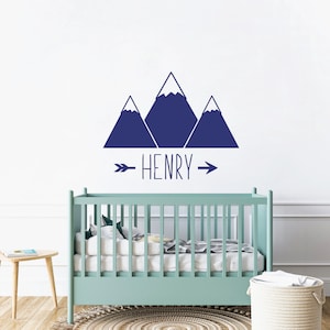 May include: A nursery wall decal with a blue mountain range design and the name "HENRY" written in a handwritten font with an arrow on either side of the name.