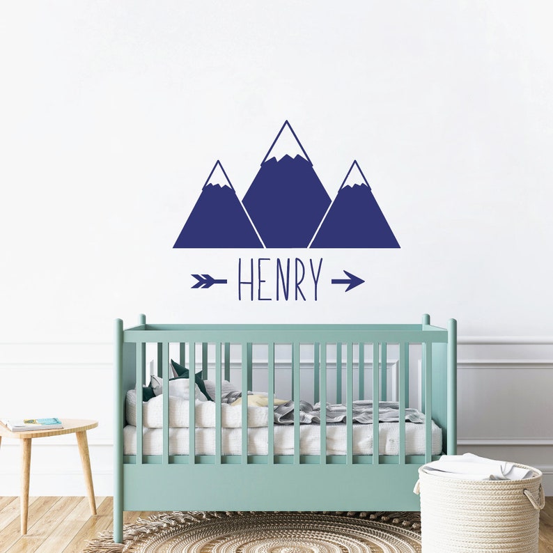 May include: A nursery wall decal with a blue mountain range design and the name "HENRY" written in a handwritten font with an arrow on either side of the name.