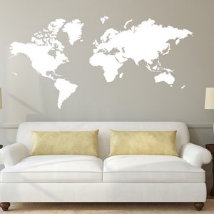May include: A white world map wall decal on a light gray wall above a white couch with two beige throw pillows. The couch is in a living room setting with two beige lamps on end tables.