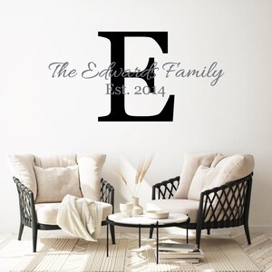 Könnte beinhalten: Schwarzer und weißer Wandaufkleber mit dem Buchstaben "E" und dem Text "The Edwards Family Est. 2014". Der Aufkleber ist an einer weißen Wand angebracht, vor der sich zwei Stühle befinden.