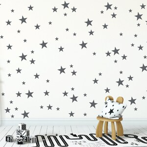 May include: A white wall with a pattern of gray stars of various sizes. A small wooden stool with a gray and white patterned cushion sits in front of the wall. A black and white patterned rug is on the floor.