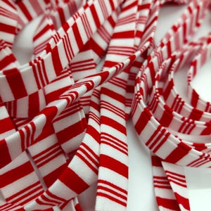 May include: A continuous length of woven fabric ribbon featuring a repeating pattern of bold red stripes alternating with thinner red and white pinstripes on a white background, coiled in multiple overlapping loops and folds.