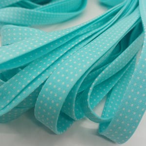 May include: Close-up of turquoise bias tape with a white polka dot pattern. The fabric is folded and layered, creating a textured effect. This tape is suitable for various sewing and crafting projects.