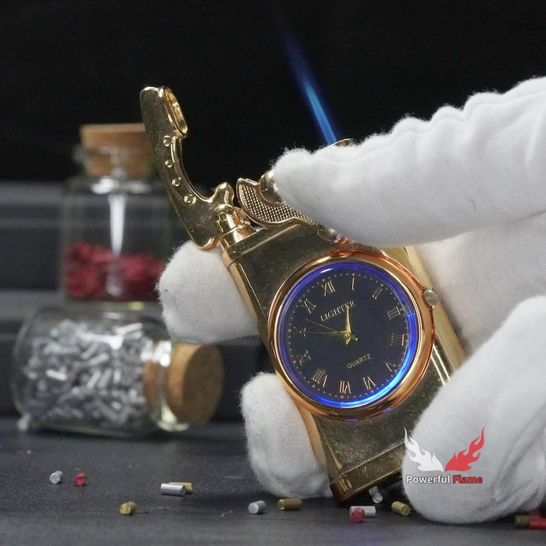 May include: A gold-tone lighter with a built-in watch face. The watch face has black Roman numeral hour markers and a blue background. The lighter is lit and has a blue flame.
