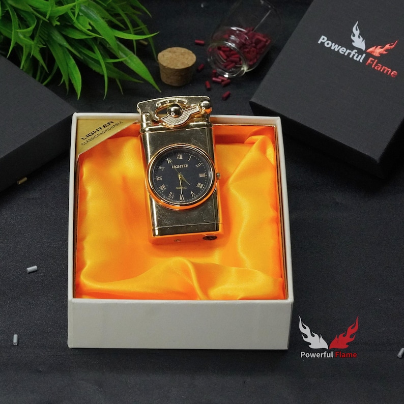May include: A gold-coloured lighter with a built-in watch. The lighter is in a white box with a yellow satin lining. The box has the text "LIGHTER CLASSIC & FUNCTIONAL" printed on the side. The lighter is a unique and stylish gift for any occasion.