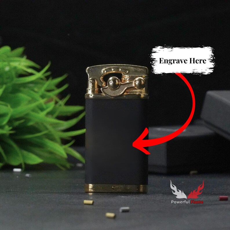 May include: Black and gold lighter with a gold top and a black body. The lighter has a space for engraving on the front. The text "Engrave Here" is written above the lighter.