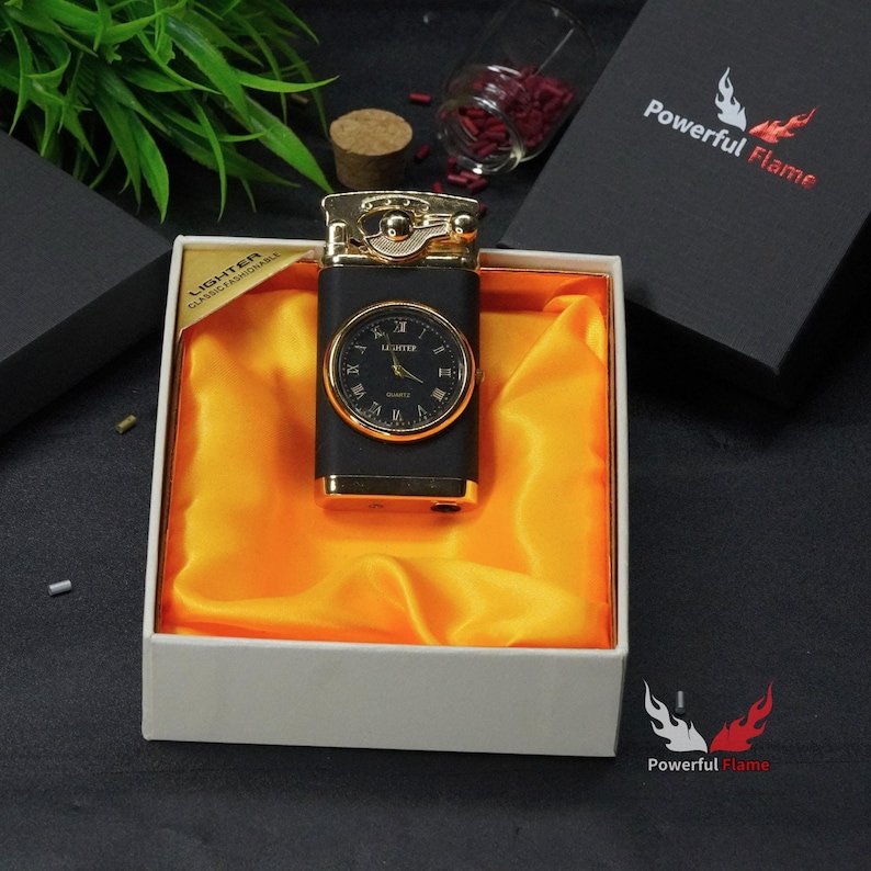 May include: A black and gold lighter with a watch face on the front. The lighter is in a white box with a yellow satin lining. The box has the words "LIGHTER CLASSICAL FASHIONABLE" printed on the side. The box is sitting on a black surface.