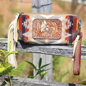 May include: A rectangular clutch bag featuring a multi-colored geometric pattern in shades of red, orange, gray, and black. The center has a rectangular leather patch with an embossed floral design and the text ZIBAGE. Includes a leather wrist strap.