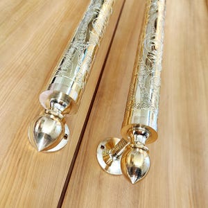 May include: A pair of gold door handles with intricate floral designs. The handles are made of metal and have a polished finish.