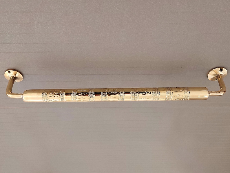 K&ouml;nnte beinhalten: Ein verziertes, goldfarbenes Handlauf aus Metall. Der Handlauf ist mit zwei Halterungen an einer Wand befestigt.
