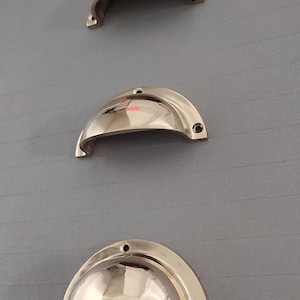 Może przedstawiać: Trzy polerowane mosiężne gałki do szafek o zaokrąglonym, kopułowym kształcie. Gałki są ułożone pionowo na szarym tle.