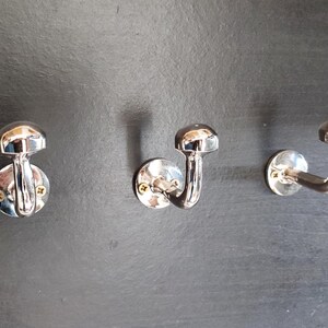 Peut inclure: Trois crochets en m&eacute;tal argent&eacute; avec un sommet arrondi et un crochet incurv&eacute;. Les crochets sont mont&eacute;s sur un mur gris fonc&eacute;.