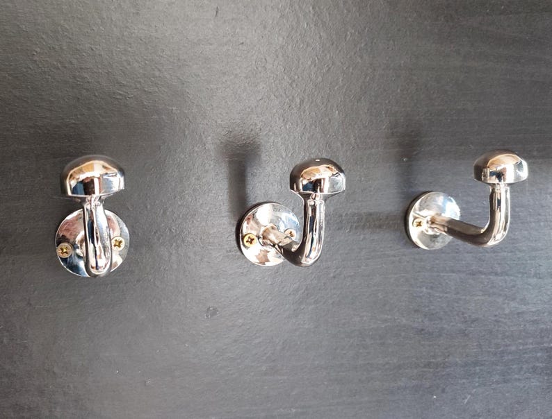 Peut inclure: Trois crochets en m&eacute;tal argent&eacute; avec un sommet arrondi et un crochet incurv&eacute;. Les crochets sont mont&eacute;s sur un mur gris fonc&eacute;.