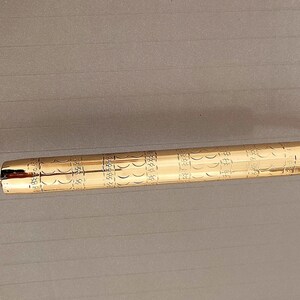 K&ouml;nnte beinhalten: Ein goldfarbener T&uuml;rgriff mit einem verzierten Design. Der Griff ist aus Metall und hat eine gebogene Form. Er ist mit Schrauben an einer Wand befestigt.