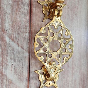 Könnte beinhalten: Ein goldfarbener Türklopfer mit einem sternförmigen Design. Der Türklopfer ist aus Metall und hat komplizierte Details.