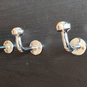 Peut inclure: Trois crochets en m&eacute;tal argent&eacute; avec des sommets arrondis mont&eacute;s sur une surface brun fonc&eacute;.