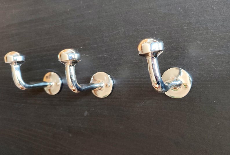 Peut inclure: Trois crochets en m&eacute;tal argent&eacute; avec des sommets arrondis mont&eacute;s sur une surface brun fonc&eacute;.