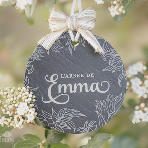 Peut inclure: Une plaque en ardoise noire avec un motif floral blanc et le texte "L'ARBRE DE Emma" suspendue à une branche d'arbre.