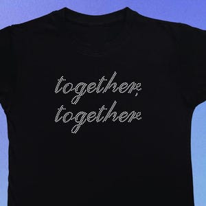 May include: Black t-shirt featuring the text "together, together" in a cursive font, made of small, sparkling rhinestones. The shirt has a crew neck and short sleeves. The brand name "jen's jems" is at the bottom left.