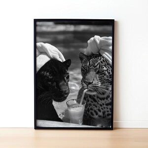 May include: Black and white photo of two animals, a black panther and a leopard, wearing white towels on their heads. They are both drinking from a glass with a straw.