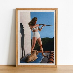 May include: A woman in a white bikini holds a rifle and aims it towards the right side of the frame. A small dog is lying on a blue and white striped blanket in the foreground. The background is a blue sky with a green hillside.