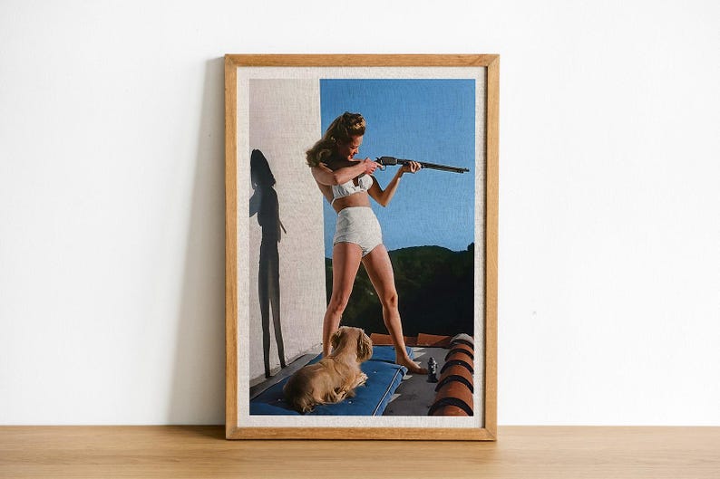 May include: A woman in a white bikini holds a rifle and aims it towards the right side of the frame. A small dog is lying on a blue and white striped blanket in the foreground. The background is a blue sky with a green hillside.
