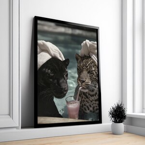 Peut inclure: Impression d'art encadr&eacute;e repr&eacute;sentant une panth&egrave;re noire et un l&eacute;opard dans une piscine, partageant une boisson rose avec une paille. La panth&egrave;re noire est &agrave; gauche, le l&eacute;opard &agrave; droite, tous deux avec des serviettes blanches. L'image est dans un cadre noir.