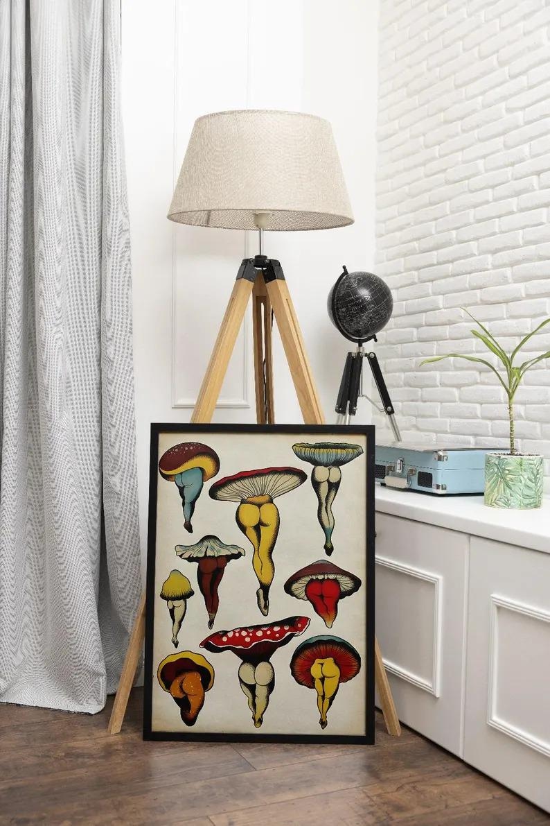 May include: A framed art print featuring whimsical mushroom illustrations with human-like legs and colorful caps. The artwork is displayed on a wooden easel in a room with a white brick wall and a floor lamp.