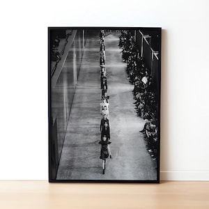 Può includere: Fotografia in bianco e nero di una lunga fila di persone che camminano lungo un corridoio. Le persone indossano tutte abiti scuri e camminano in fila indiana. Il corridoio è fiancheggiato da muri su entrambi i lati.