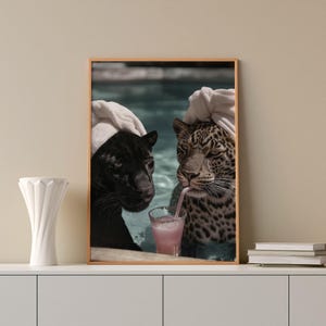 Peut inclure: Impression encadr&eacute;e repr&eacute;sentant deux grands f&eacute;lins, une panth&egrave;re noire et un l&eacute;opard, se relaxant dans une piscine. Les deux animaux portent des serviettes blanches sur la t&ecirc;te. Le l&eacute;opard boit une boisson rose.