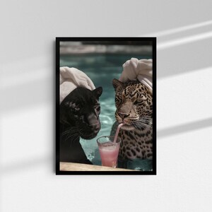 Peut inclure: Impression d'art encadr&eacute;e repr&eacute;sentant une panth&egrave;re noire et un l&eacute;opard dans une piscine, chacun avec une serviette sur la t&ecirc;te. Le l&eacute;opard boit une boisson rose avec une paille. L'&oelig;uvre est affich&eacute;e sur un mur blanc.
