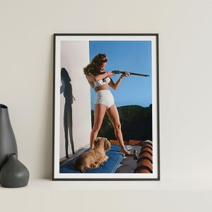 May include: A woman in a white bikini holds a rifle and aims it towards the right side of the frame. She is standing on a patio with a small dog lying on a blue cushion. The background is a blue sky with some trees in the distance.