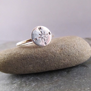 May include: A silver ring with a compass design. The compass features a star in the center and the letters N, S, E, and W around the edge.