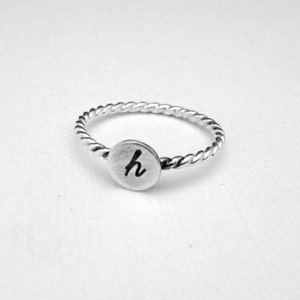May include: A silver ring with a twisted band and a round disc with the letter "h" engraved on it.